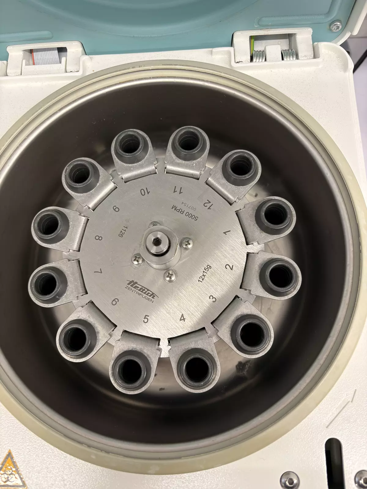 One of the stations: a benchtop centrifuge. The arm lifts the lid, turns the knob and aligns the 12-tube rotor before loading.