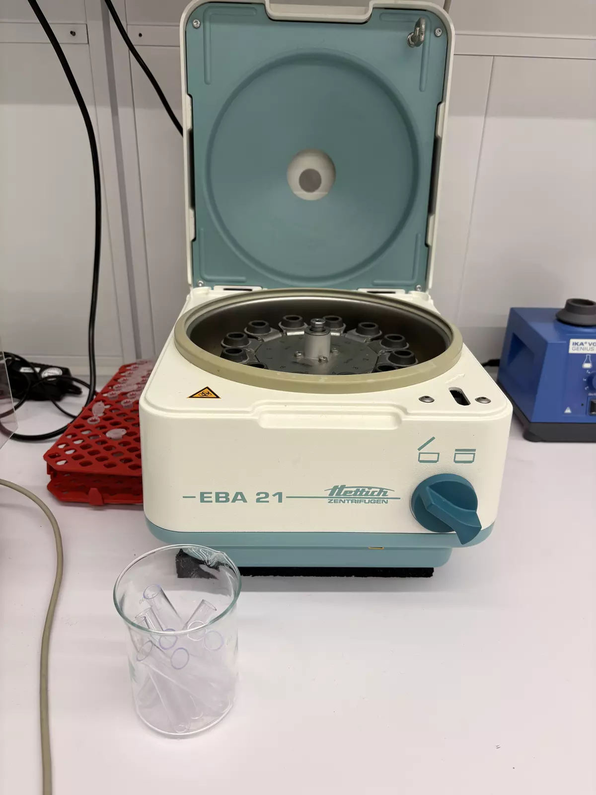 One of the stations: a benchtop centrifuge. The arm lifts the lid, turns the knob and aligns the 12-tube rotor before loading.